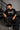 Man wearing a black STAR BOY oversized t-shirt with "Hot Wheels" graphics, sitting on a black couch. Streetwear fashion.