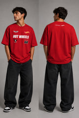Man wearing a black STAR BOY oversized t-shirt with "Hot Wheels" graphics, sitting on a black couch. Streetwear fashion. - red