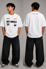 Man wearing a black STAR BOY oversized t-shirt with "Hot Wheels" graphics, sitting on a black couch. Streetwear fashion. - white