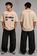 Man wearing a black STAR BOY oversized t-shirt with "Hot Wheels" graphics, sitting on a black couch. Streetwear fashion. - beige