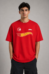 Couple wearing matching red oversized Hot Wheels t-shirts and black bottoms, standing on stairs. Feature iconic Hot Wheels logo. - red