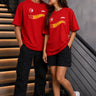 Couple wearing matching red oversized Hot Wheels t-shirts and black bottoms, standing on stairs. Feature iconic Hot Wheels logo.