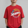 Model wearing a black oversized t-shirt with a vintage Hot Wheels graphic and flames. The tee has a relaxed fit and is paired with black pants. - red