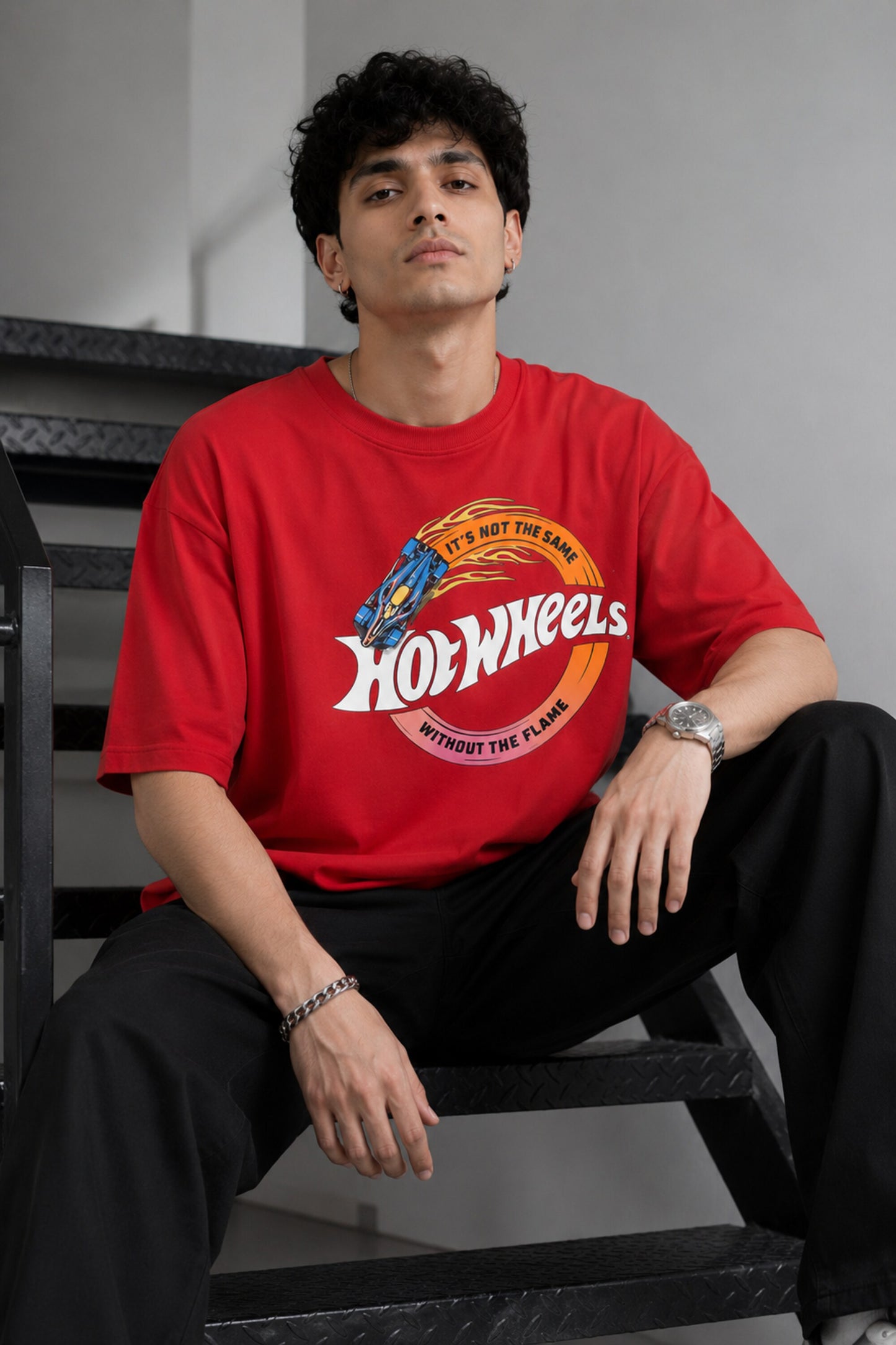 Model wearing a black oversized t-shirt with a vintage Hot Wheels graphic and flames. The tee has a relaxed fit and is paired with black pants.