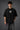 Couple wearing black Iron Man Jarvish oversized t-shirts. Man's back shows "IRON MAN" logo. Woman's front shows Iron Man arc reactor logo. Dark grey background.