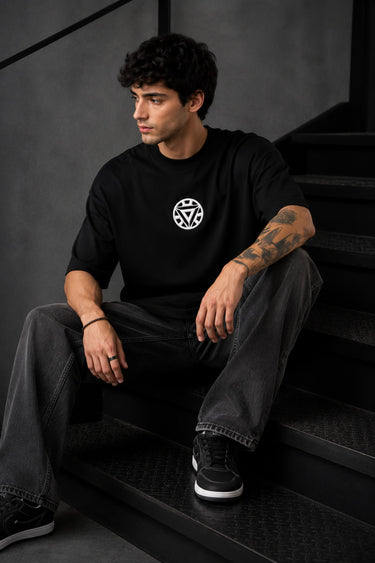 Couple wearing black Iron Man Jarvish oversized t-shirts. Man's back shows "IRON MAN" logo. Woman's front shows Iron Man arc reactor logo. Dark grey background.