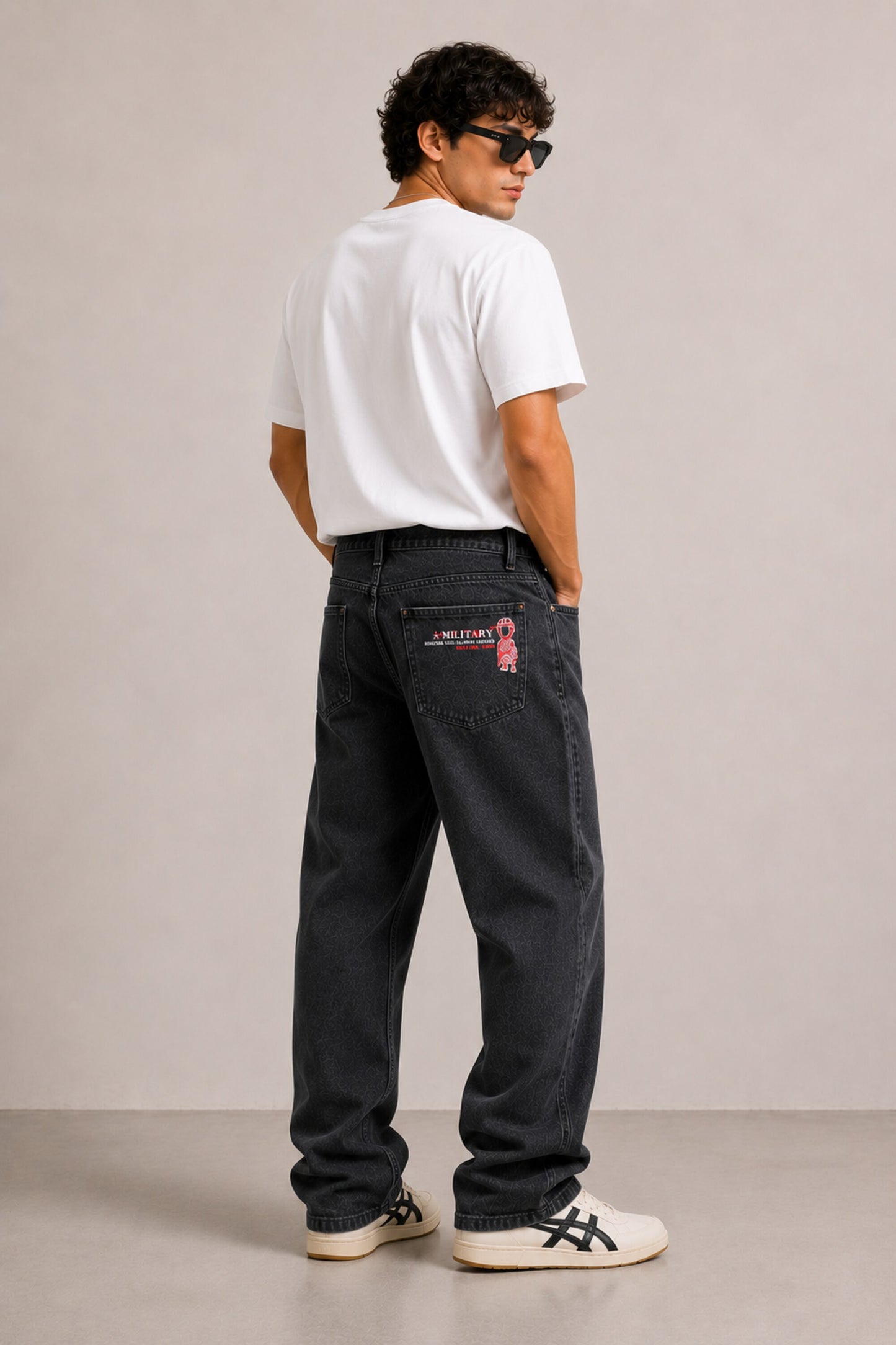 Person wearing black pants with a brand logo, white shirt, and sneakers on a plain background