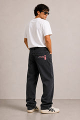 Person wearing black pants with a brand logo, white shirt, and sneakers on a plain background