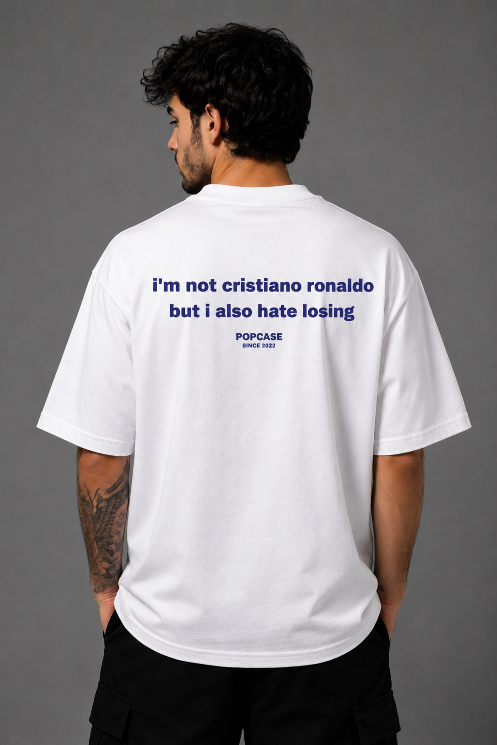 White POPCASE oversized tshirt with i'm not cristiano ronaldo but i also hate losing quote in navy on back, POPCASE Since 2022 tagline
