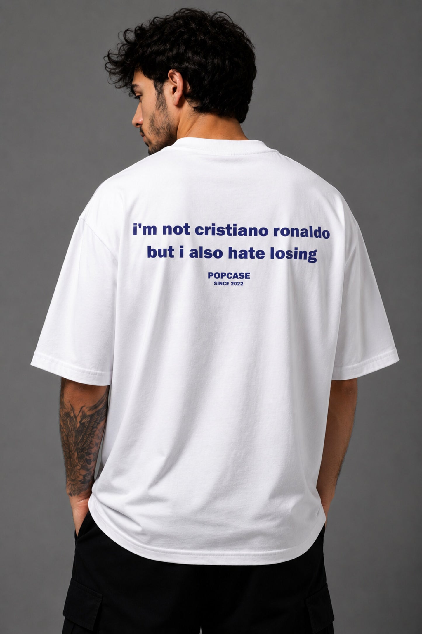 White POPCASE oversized tshirt with i'm not cristiano ronaldo but i also hate losing quote in navy on back, POPCASE Since 2022 tagline