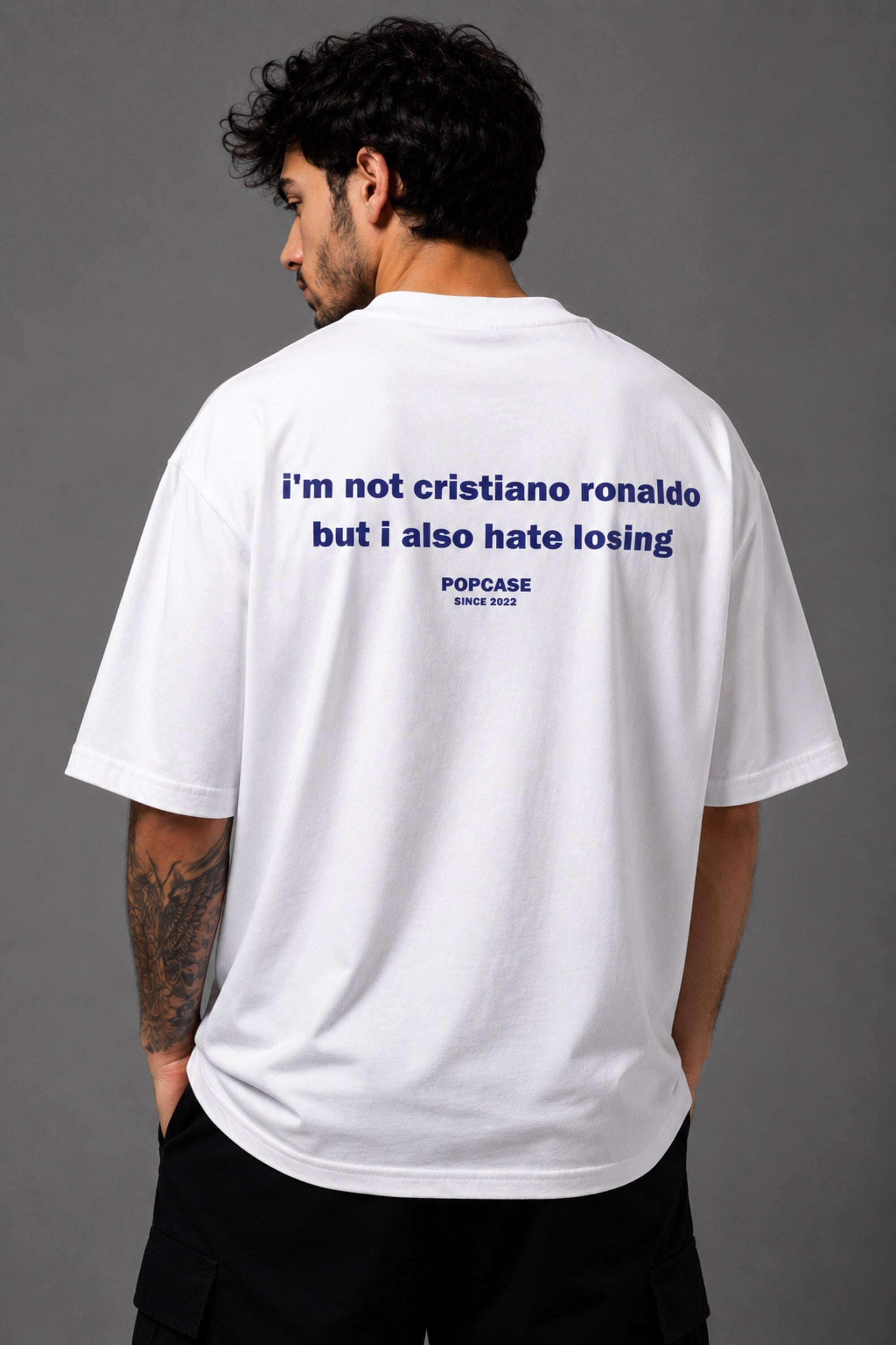 White POPCASE oversized tshirt with i'm not cristiano ronaldo but i also hate losing quote in navy on back, POPCASE Since 2022 tagline