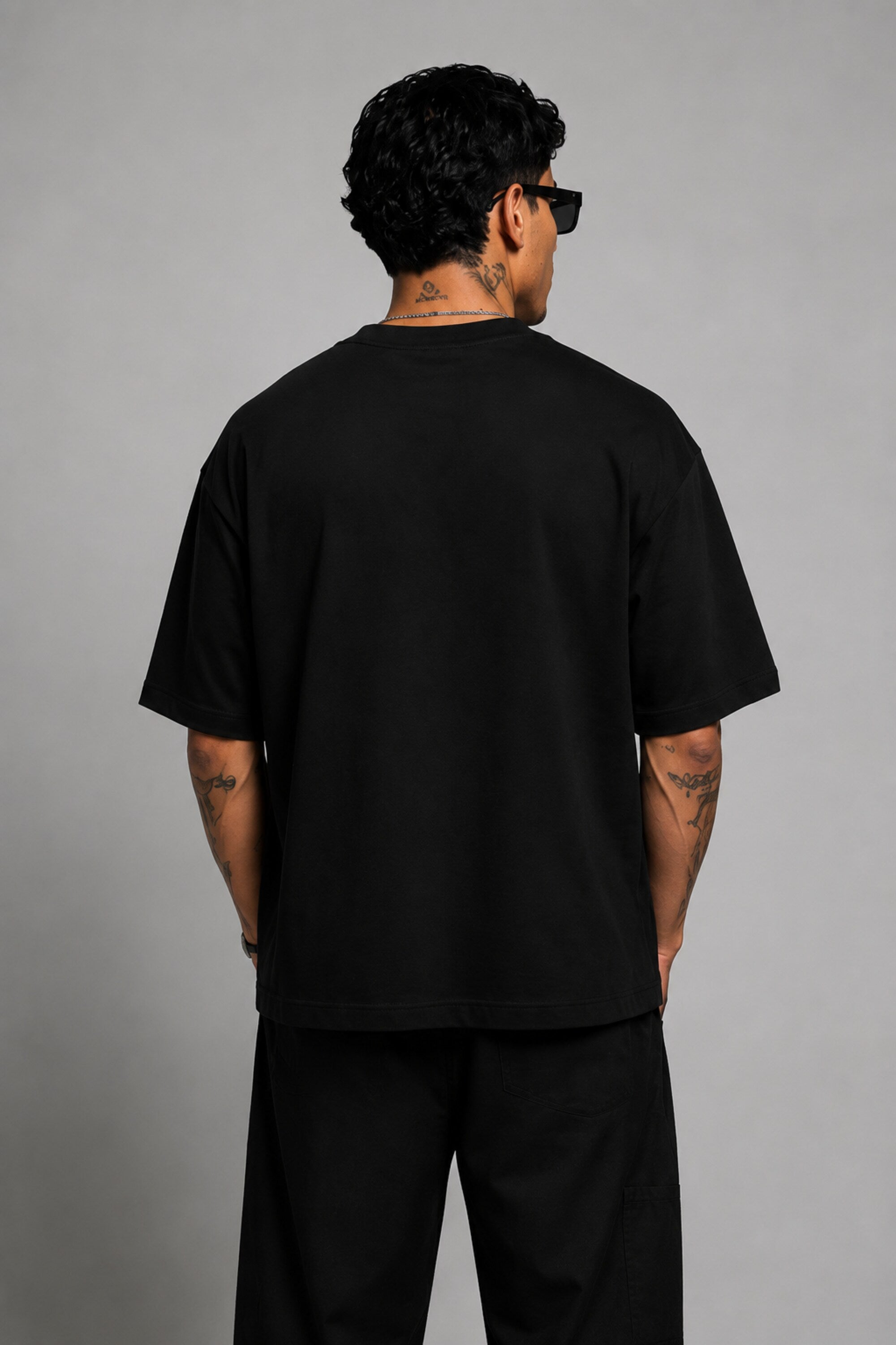 Man wearing a black oversized t-shirt with a red 'SPIDERMAN' puff print graphic and a red spider logo on the side. Model is wearing sunglasses and cargo pants.