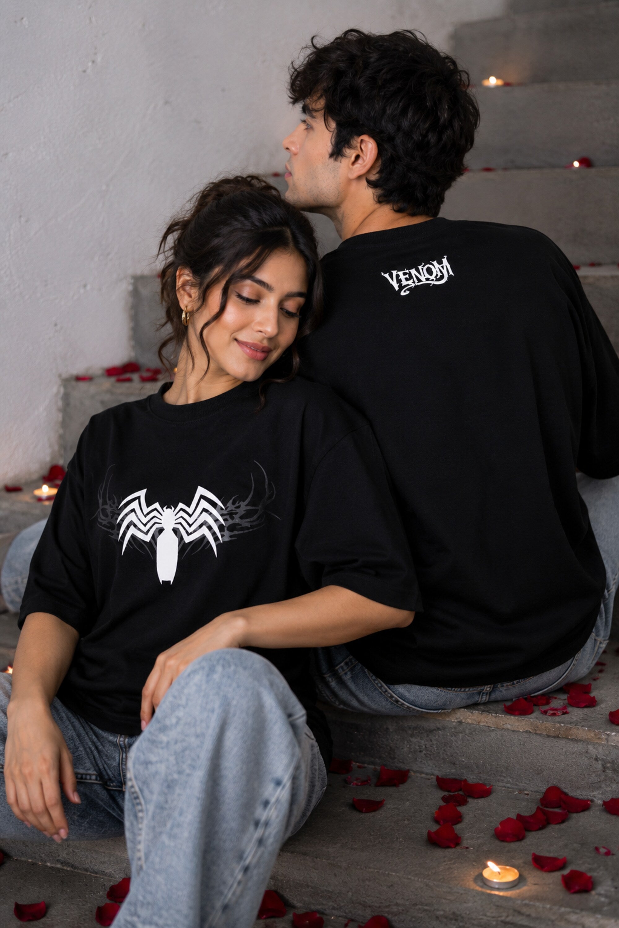 Two people sitting on steps with black shirts featuring spider-like designs.