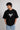 Person wearing a black t-shirt with a white spider logo on a plain background
