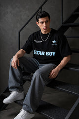 Black STAR BOY oversized t-shirt with a light blue raised graphic of a star and text. Detailed fabric texture shown.