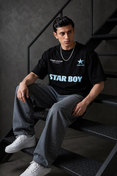 Black STAR BOY oversized t-shirt with a light blue raised graphic of a star and text. Detailed fabric texture shown.