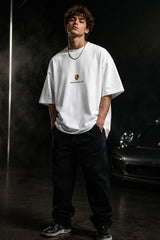 Person wearing a white t-shirt with a logo in a dark setting with a car in the background