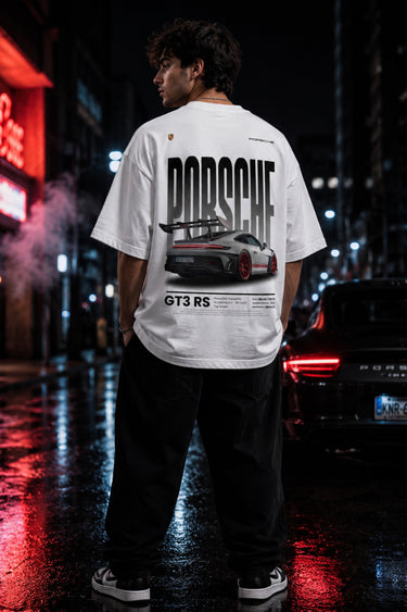 Person wearing a white Porsche t-shirt with a car graphic on a city street at night.