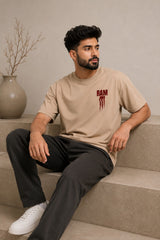 Model wearing a beige RAM oversized t-shirt with a red graphic print on the chest, paired with dark trousers and white sneakers. Showcases streetwear style and premium comfort.