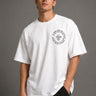 Man wearing a white RAM YODHA oversized t-shirt with 'Ram' graphic on front and Ram Yoddha artwork on back, seated on wooden steps. - white