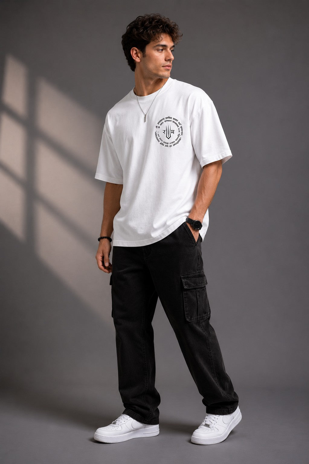 Man wearing a white RAM YODHA oversized t-shirt with 'Ram' graphic on front and Ram Yoddha artwork on back, seated on wooden steps.