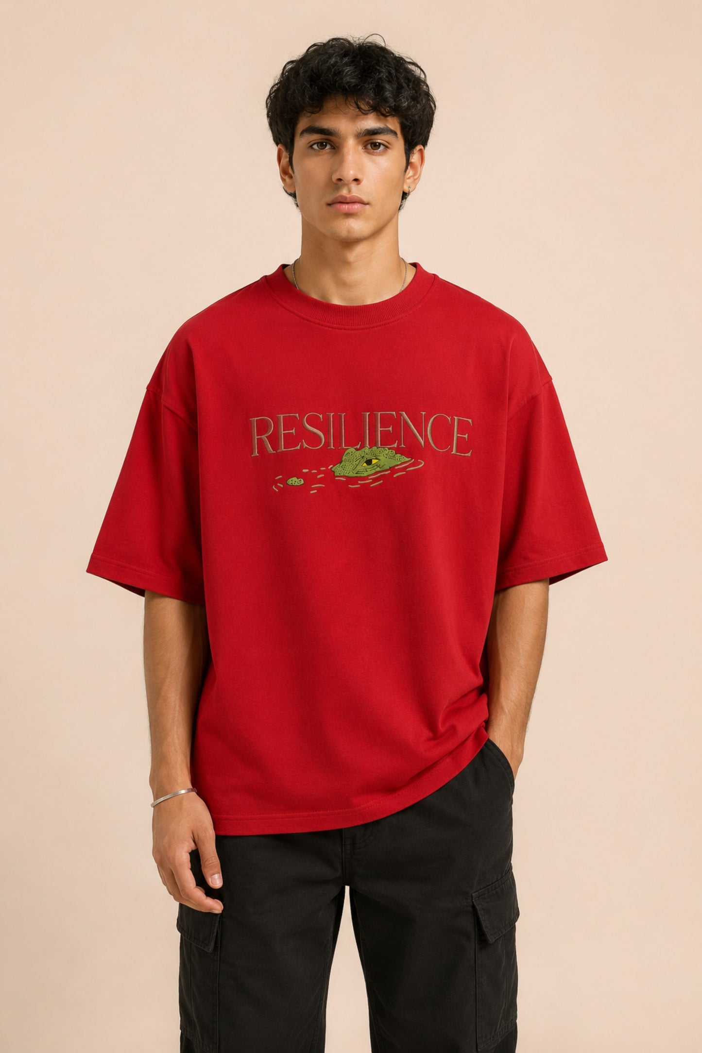 Red oversized t-shirt with "RESILIENCE" embroidered in gold and a green embroidered crocodile graphic. Features a ribbed neckline and premium stitching. - red
