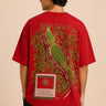 Red oversized t-shirt with "RESILIENCE" embroidered in gold and a green embroidered crocodile graphic. Features a ribbed neckline and premium stitching.