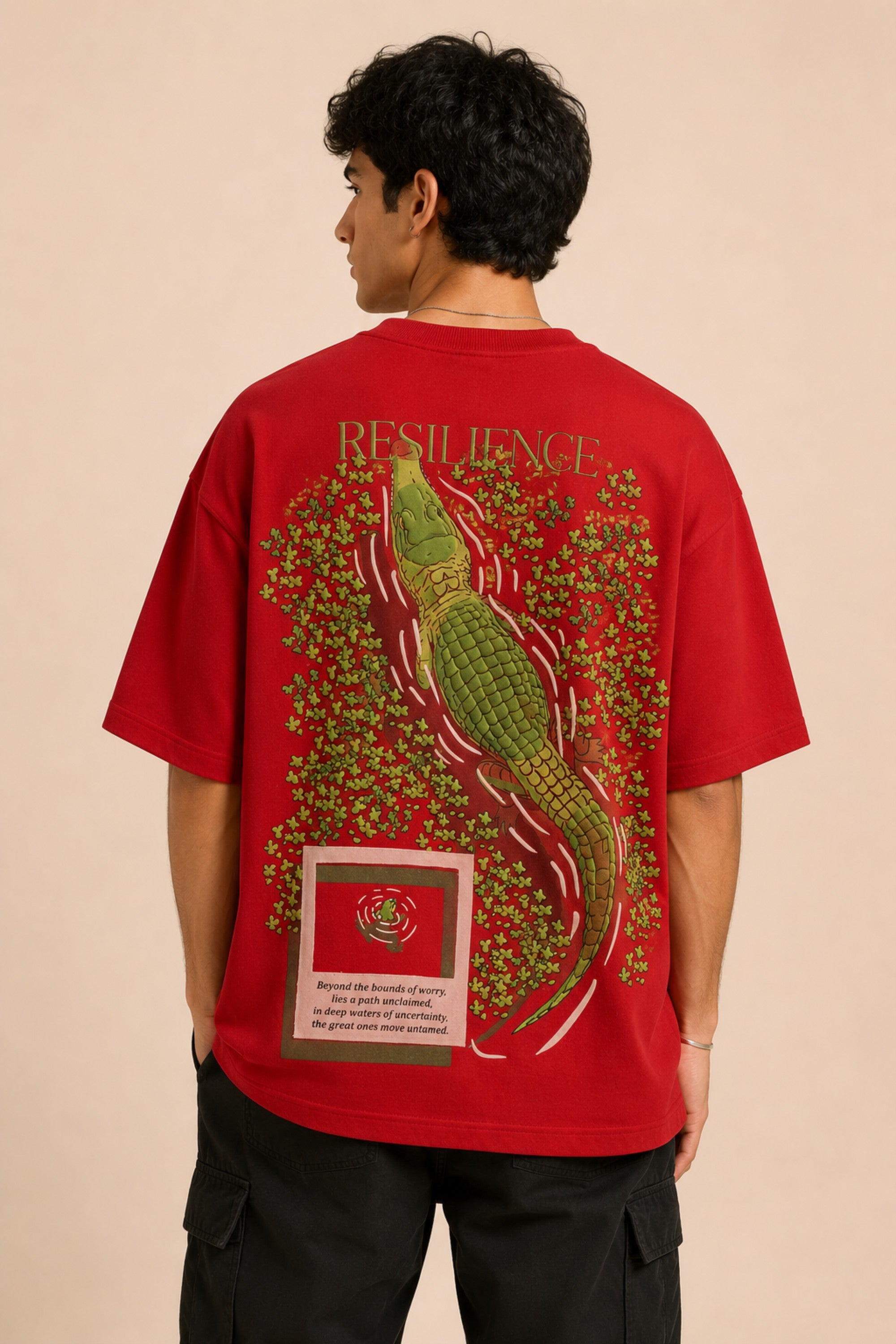 Red oversized t-shirt with "RESILIENCE" embroidered in gold and a green embroidered crocodile graphic. Features a ribbed neckline and premium stitching.