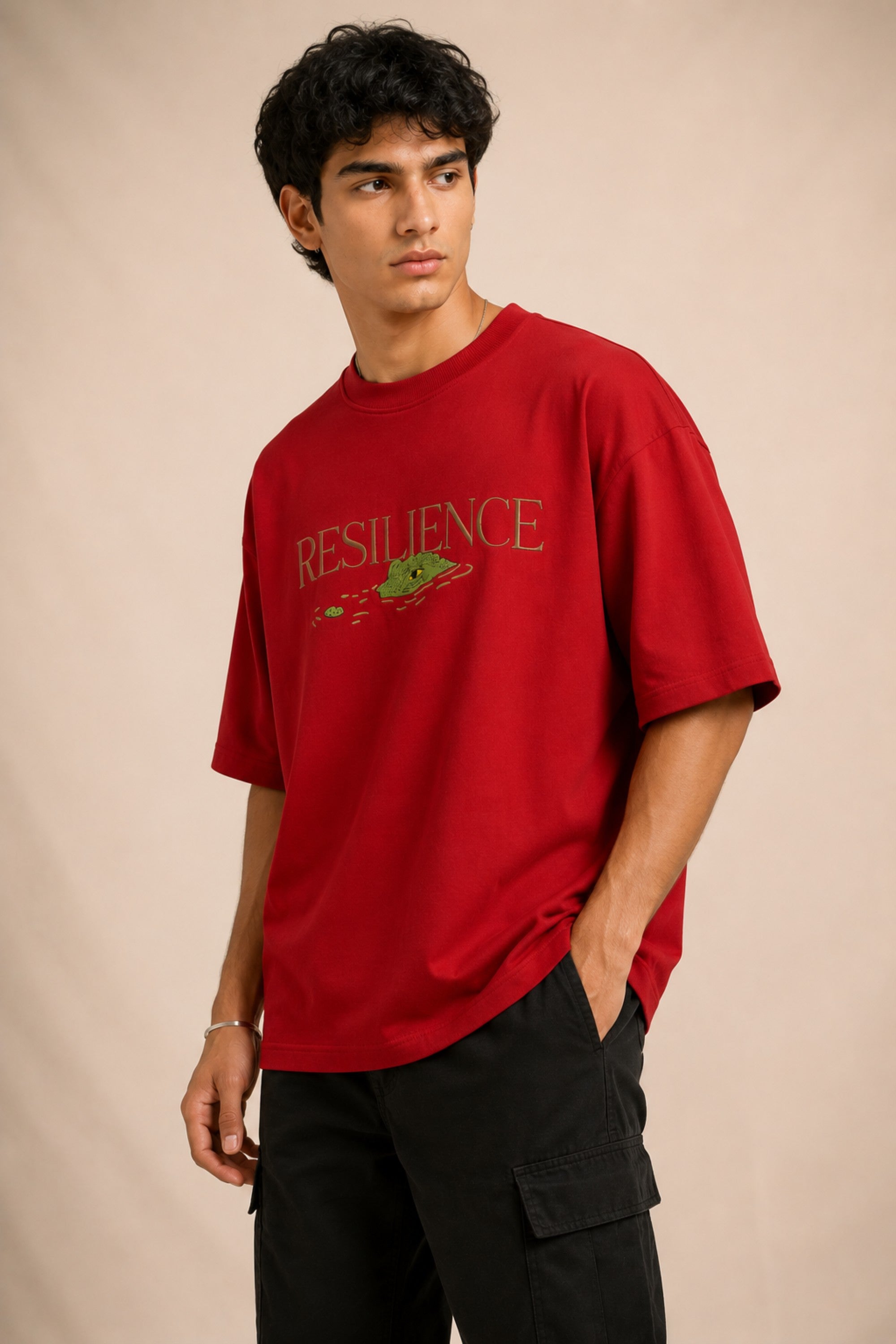 Red oversized t-shirt with "RESILIENCE" embroidered in gold and a green embroidered crocodile graphic. Features a ribbed neckline and premium stitching.
