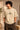 Close-up of a Rooted oversized t-shirt in beige, featuring a dark green circular graphic of a tree of life with tribal figures, and text 'in the rhfym of life'.