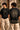 Close-up of a Rooted oversized t-shirt in beige, featuring a dark green circular graphic of a tree of life with tribal figures, and text 'in the rhfym of life'. - black
