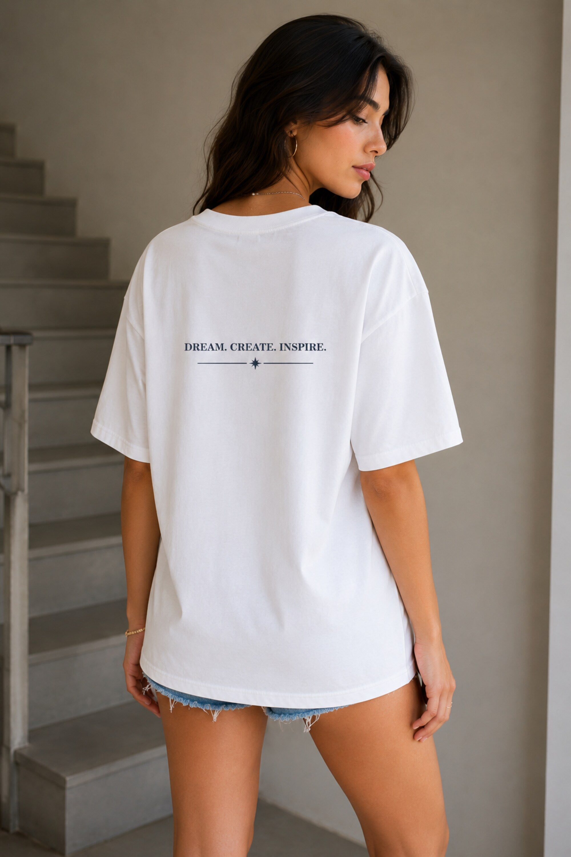 Woman wearing a white t-shirt with text on the back, standing in a neutral indoor setting.
