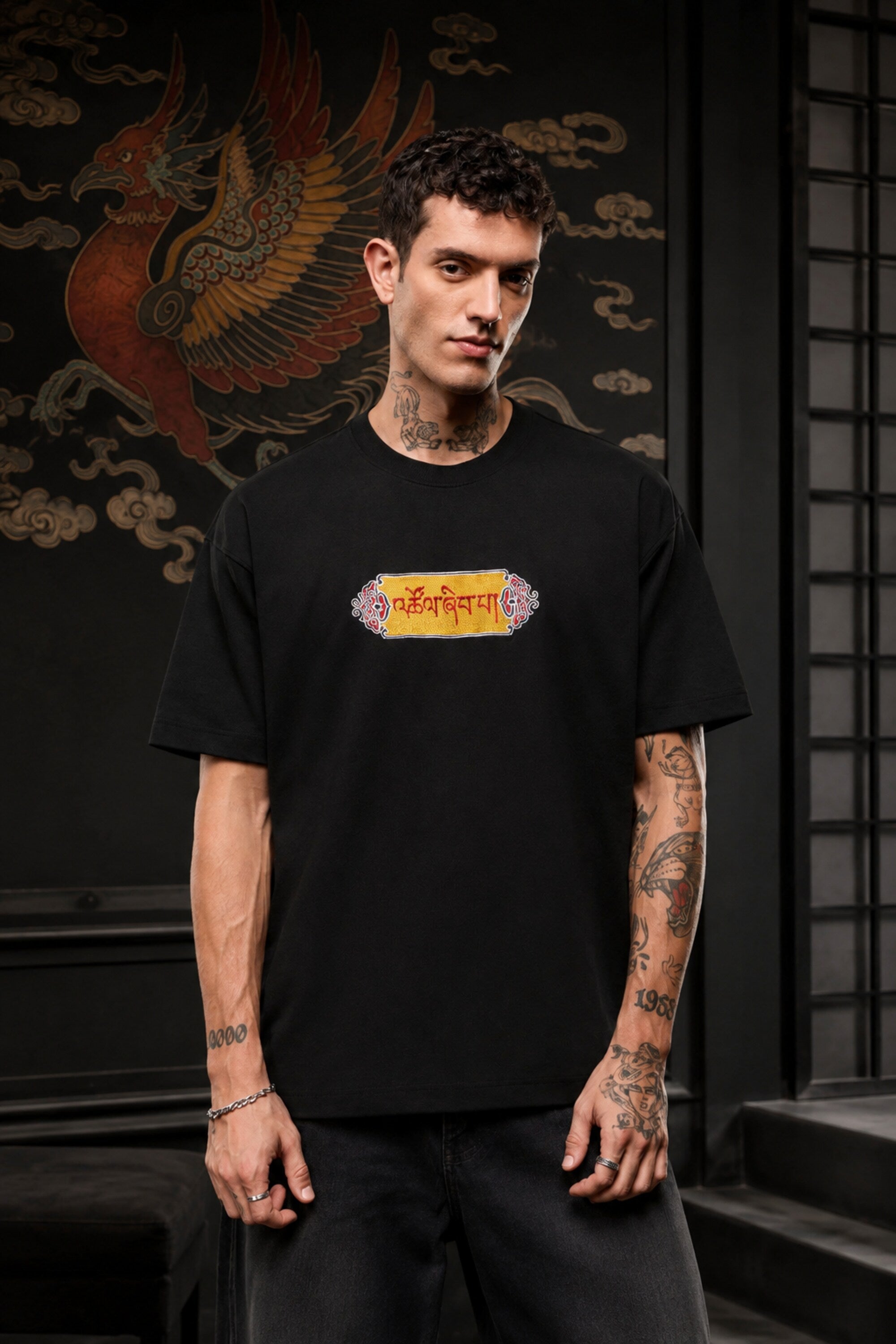 Black oversized t-shirt with Tibetan script in red on golden decorative banner, spiritual streetwear India - black