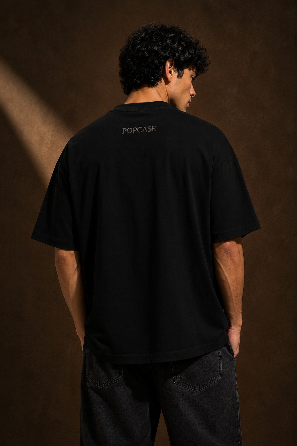 Back view of a man wearing a black UNBREAKABLE TIGER oversized t-shirt, featuring a subtle tonal logo on the upper back. Streetwear aesthetic.