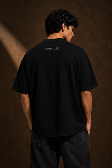 Back view of a man wearing a black UNBREAKABLE TIGER oversized t-shirt, featuring a subtle tonal logo on the upper back. Streetwear aesthetic.