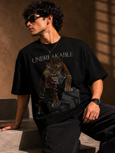 Back view of a man wearing a black UNBREAKABLE TIGER oversized t-shirt, featuring a subtle tonal logo on the upper back. Streetwear aesthetic.