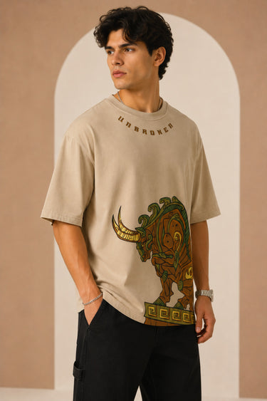 Unbroken Design oversized t-shirt in a beige hue featuring a detailed, stylized brown and green bull graphic print and "UNBROKEN" text across the chest. Showcases ribbed neckline.