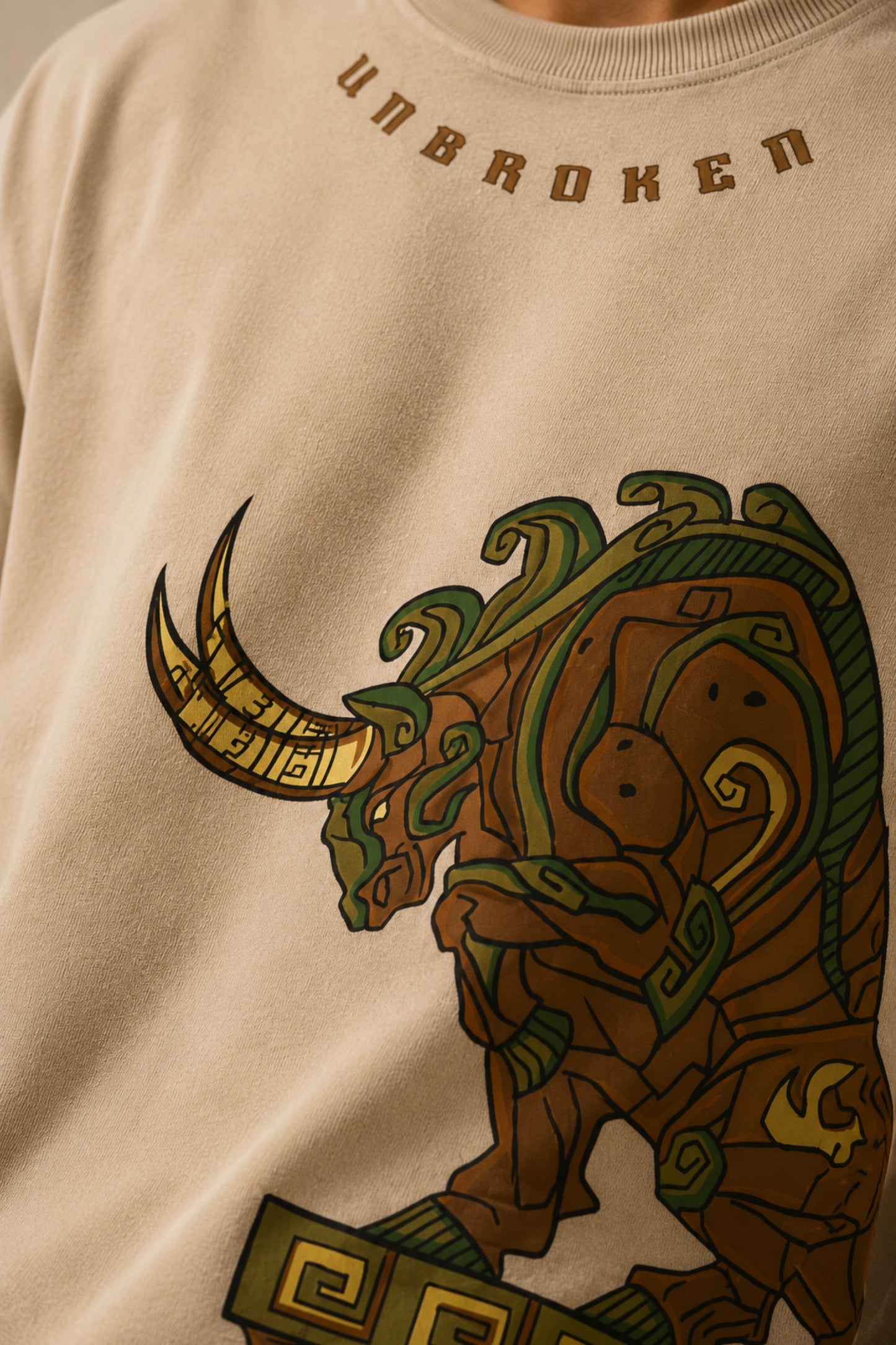Unbroken Design oversized t-shirt in a beige hue featuring a detailed, stylized brown and green bull graphic print and "UNBROKEN" text across the chest. Showcases ribbed neckline.