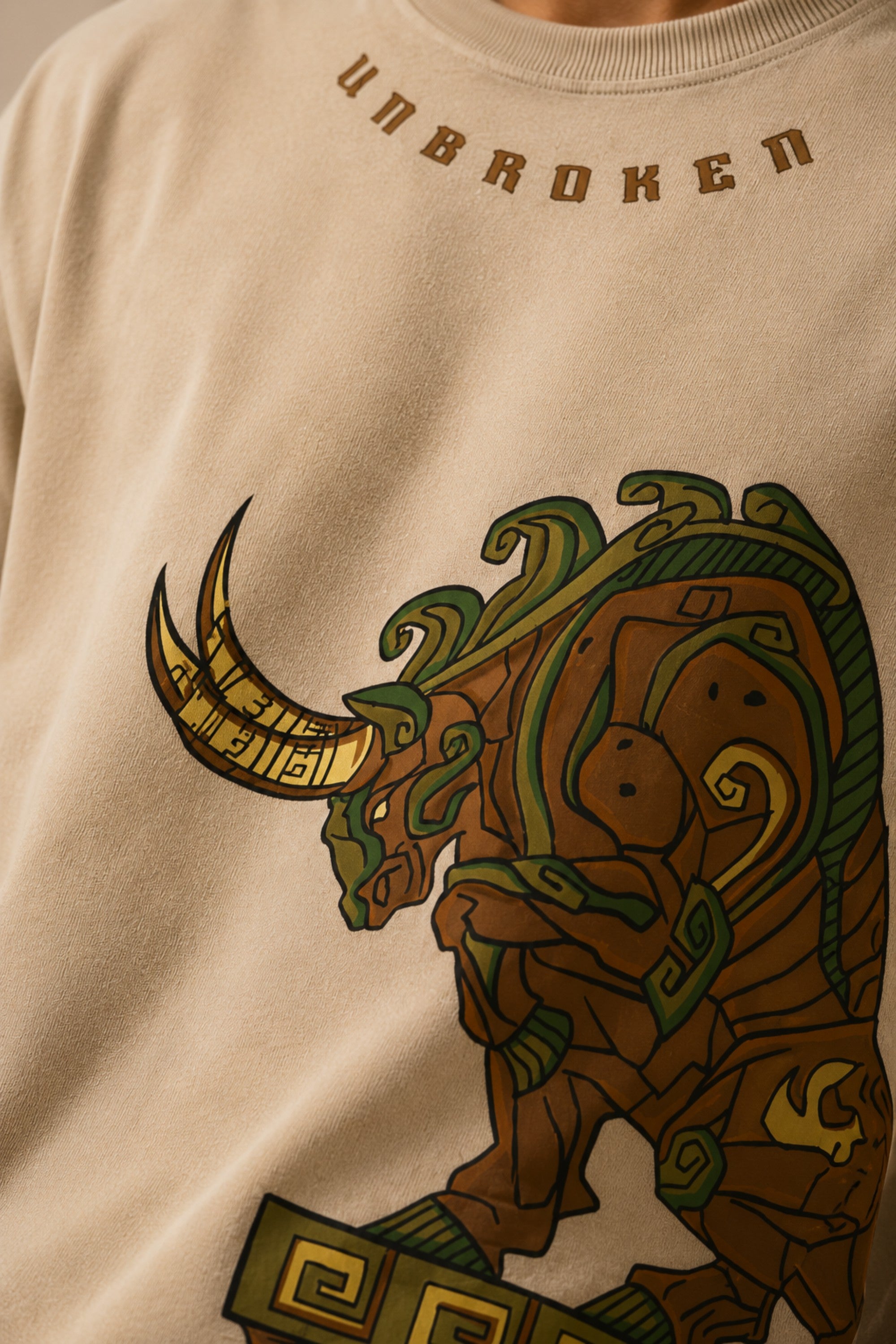 Unbroken Design oversized t-shirt in a beige hue featuring a detailed, stylized brown and green bull graphic print and "UNBROKEN" text across the chest. Showcases ribbed neckline.