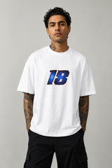 Man wearing a white VIRAT MCG 18 Vs PAK oversized t-shirt with a blue galaxy-themed '18' graphic. He is sitting on steps, showcasing the relaxed fit and streetwear style.