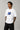 Man wearing a white VIRAT MCG 18 Vs PAK oversized t-shirt with a blue galaxy-themed '18' graphic. He is sitting on steps, showcasing the relaxed fit and streetwear style.