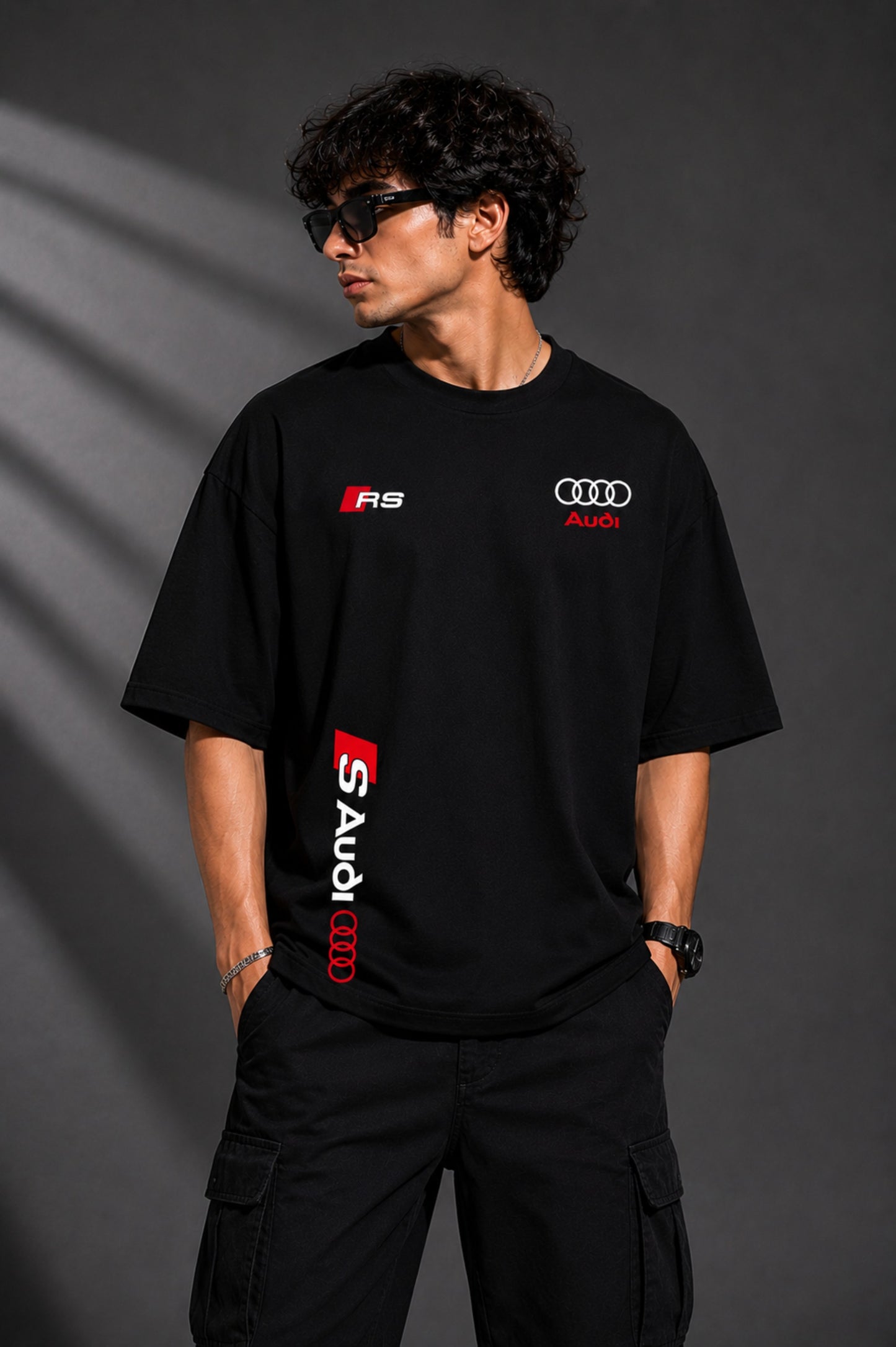 Black oversized Audi RS t-shirt with iconic white and red RS logo on the chest and Audi rings graphic. Premium fabric detail shown.