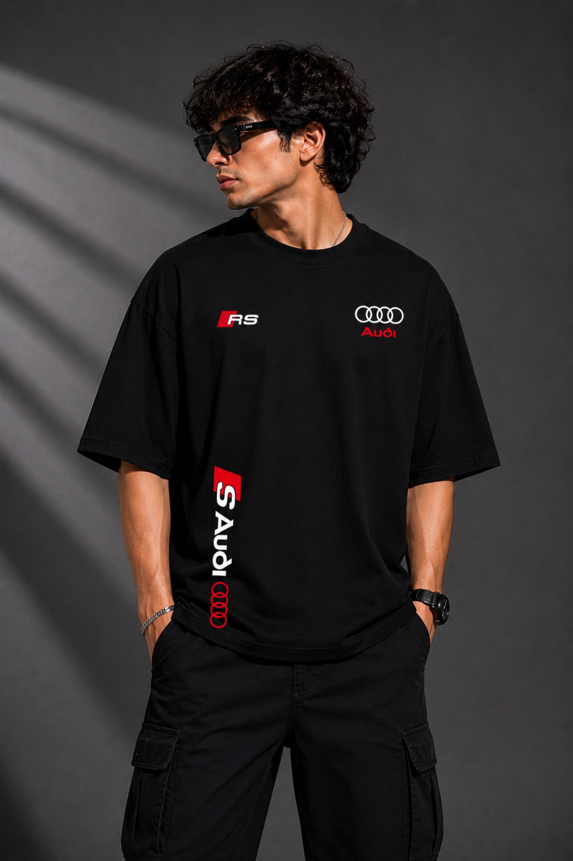 Black oversized Audi RS t-shirt with iconic white and red RS logo on the chest and Audi rings graphic. Premium fabric detail shown.