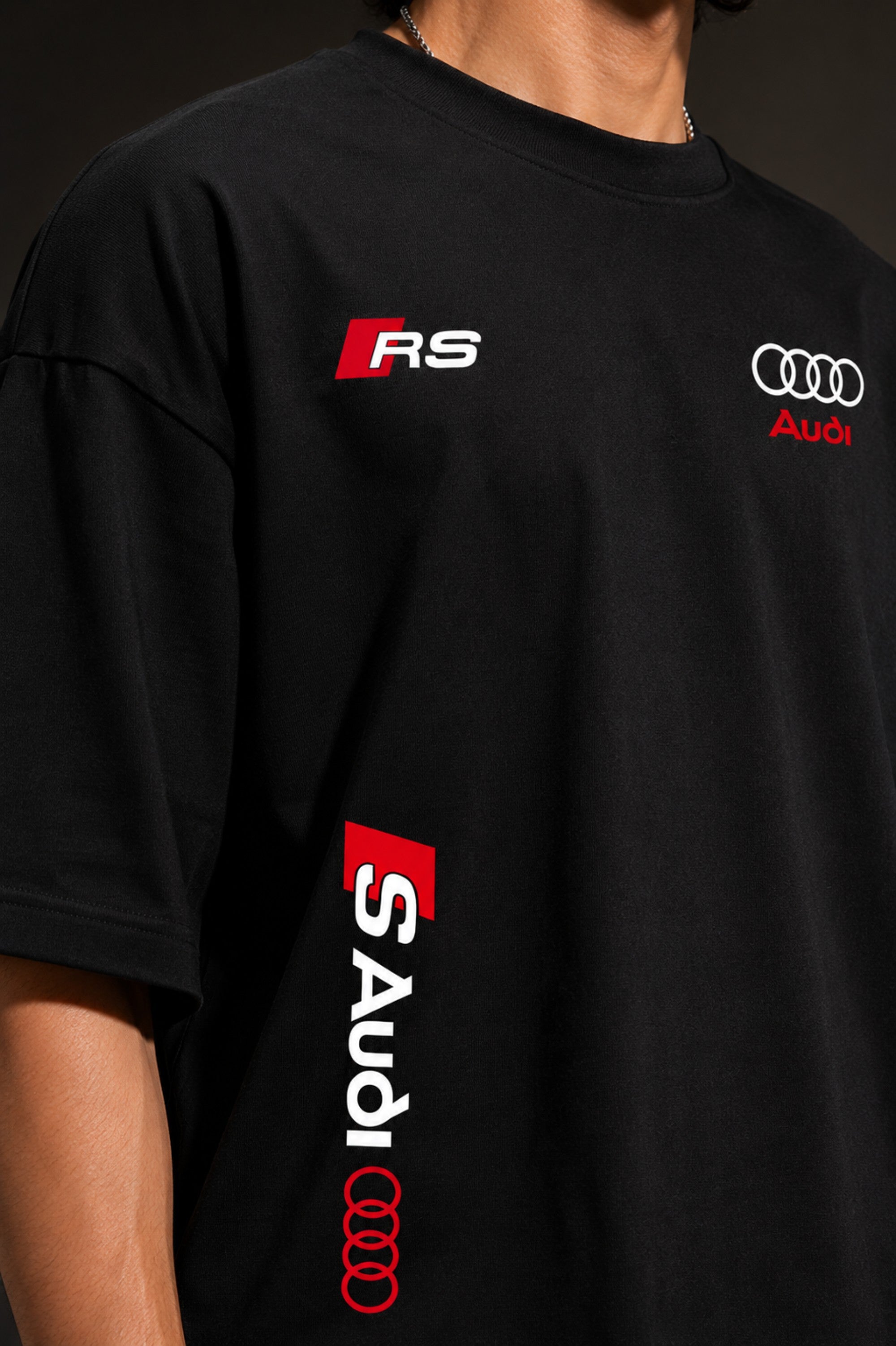 Black oversized Audi RS t-shirt with iconic white and red RS logo on the chest and Audi rings graphic. Premium fabric detail shown.