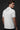 Man wearing a white polo shirt with a black bat logo on the back against a dark background