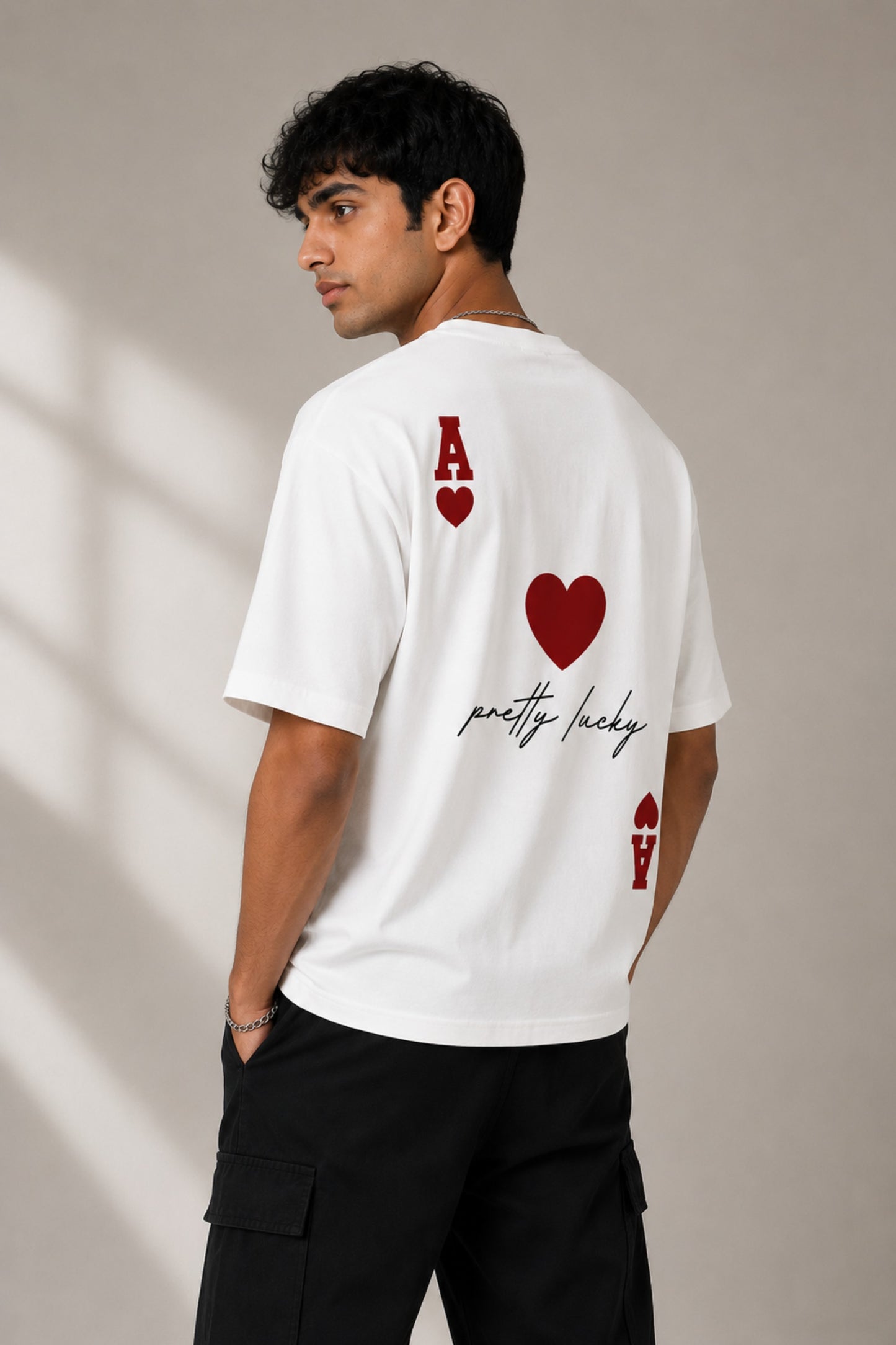 Man wearing a white oversized t-shirt with a large red Ace of Hearts graphic and 'pretty lucky' text on the back. Streetwear fashion.