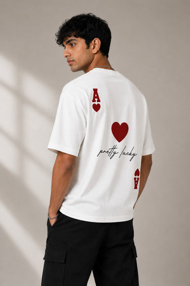 Man wearing a white oversized t-shirt with a large red Ace of Hearts graphic and 'pretty lucky' text on the back. Streetwear fashion.