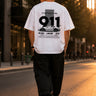 Person wearing a white t-shirt with Porsche 911 design walking on a street at sunset.
