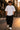 Person wearing a white t-shirt with '911' logo and black pants on a city street.
