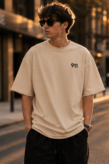 Person wearing a beige t-shirt with '911' logo on a street.